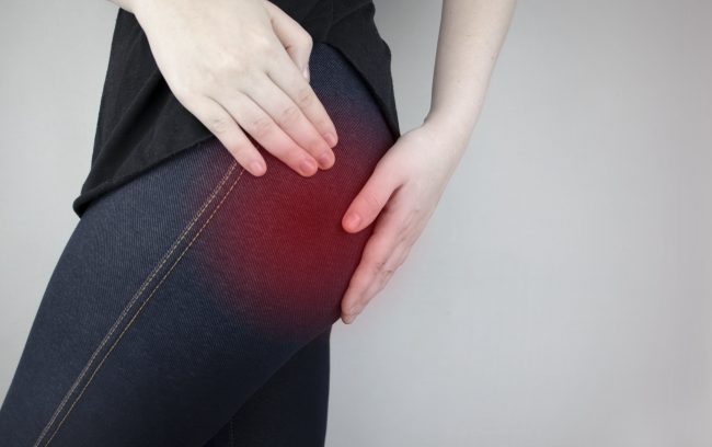 A woman showing discomfort in her lower, posterior pelvic region by holding the area with her hands. The area is colored red to show it is inflamed, possibly from sciatica